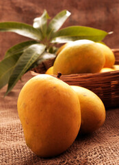 Wall Mural - Mango fruits in wooden basket with leaf after harvest from farm, Mango fruits with leaf on Jute background.