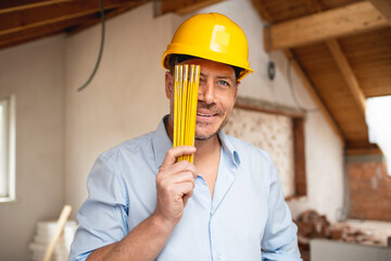 Architect with yellow safety helmet, blue shirt and jeans checks construction progress on building site in loft, attic with a yellow  folding rule