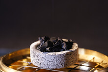 Closeup Of A White Ashtray With Black Ash On A Fire Netting