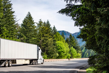 White commercial long haul freight big rig semi truck transporting cargo in dry van semi trailer driving on the one way highway green road