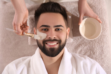 Sticker - Cosmetologist applying mask on man's face in spa salon, top view