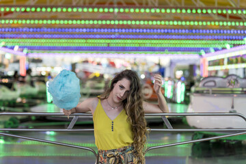 Wall Mural - Attractive young female standing with cotton candy in hand and spending time in an amusement park