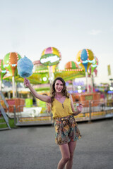 Wall Mural - Attractive young female standing with cotton candy in hand and spending time in an amusement park