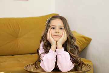 Cute little girl sitting on a sofa with hands under her head