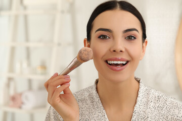 Canvas Print - Beautiful young woman applying face powder with brush in bathroom at home