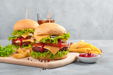 Delicious homemade burgers, French fries and cola on a gray background with space to copy.