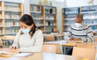 © JackF - Interested young Latina in medical face mask spending time in library during coronavirus pandemic, reading books and making notes. Compelled precautions concept