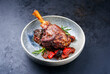 Modern style traditional braised slow cooked lamb shank in red wine sauce with eggplants and tomatoes served as close-up in a design bowl