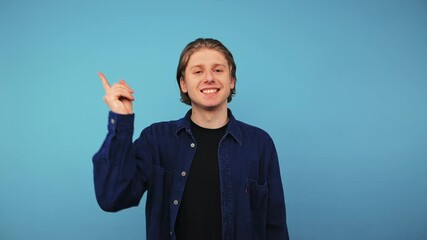 Wall Mural - Positive guy in a blue shirt is isolated against the background of a globe wall, looks into the camera with a smile on his face and points his finger to the side.