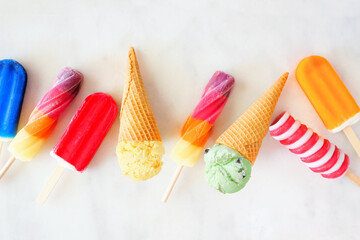 Wall Mural - Assortment of colorful summer popsicles and ice cream desserts. Above view scattered on a bright white marble background.