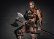 Strong redhead woman viking with axe and armour in dark background