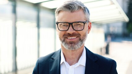 Close up portrait of happy Caucasian middle-aged stylish male traveller texting on smartphone browsing online standing in town on train station, looking at camera and smiling, traveling, business trip