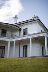 Old white historic grand house on a grass hill blue sky balcony awning 