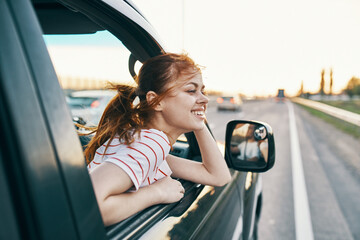 happy woman on the track peeking out of the car window in summer vacation and travel tourism