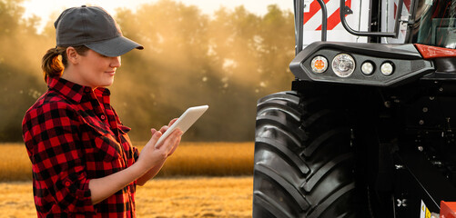 Wall Mural - Woman farmer with digital tablet on a background of harvester. Smart farming concept.	
