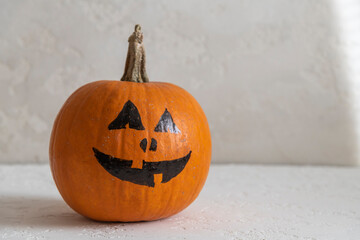 Wall Mural - Close-up view of orange Halloween pumpkin with black drawing face lying on white table. Jack O'Lantern. Side view. Homemade Halloween decoration theme.