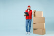 Full size body length delivery guy employee man in red cap white T-shirt vest uniform work as dealer courier hold blank cardboard box isolated on pastel blue color background studio. Service concept.