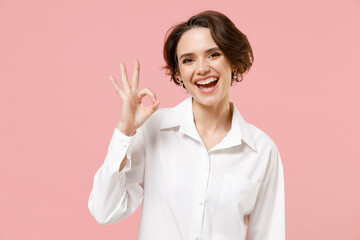 Wall Mural - Young smiling happy successful employee business woman corporate lawyer 20s in classic formal white shirt work in office show ok okay gesture isolated on pastel pink color background studio portrait.