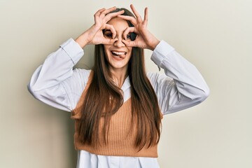 Wall Mural - Beautiful brunette young woman wearing casual clothes doing ok gesture like binoculars sticking tongue out, eyes looking through fingers. crazy expression.