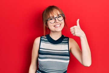 Redhead young woman wearing casual clothes and glasses smiling happy and positive, thumb up doing excellent and approval sign