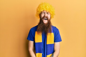 Sticker - Redhead man with long beard football hooligan cheering game wearing funny wig sticking tongue out happy with funny expression. emotion concept.