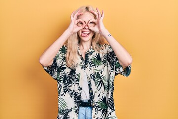 Canvas Print - Beautiful caucasian woman with blond hair wearing tropical shirt doing ok gesture like binoculars sticking tongue out, eyes looking through fingers. crazy expression.