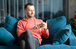 © uladzimirzuyeu - A man uses a smartphone on his home couch while relaxing at home. Applications, calls, internet concept.