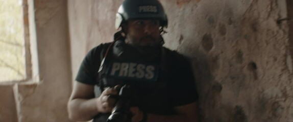 Sticker - Hispanic male war journalist wearing protective helmet and bulletproof vest gear taking photos during military operation. Shot with 2x anamorphic lens