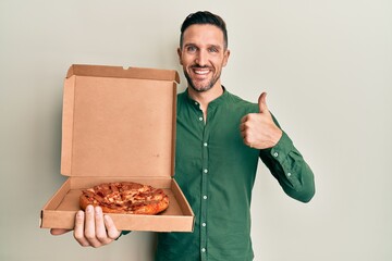 Sticker - Handsome man with beard holding italian pizza smiling happy and positive, thumb up doing excellent and approval sign