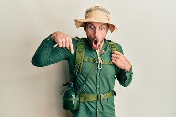 Poster - Handsome man with beard wearing explorer hat and backpack pointing down with fingers showing advertisement, surprised face and open mouth