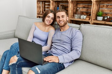 Young caucasian couple using laptop sitting on the sofa at home.