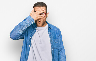 Wall Mural - Young caucasian man wearing casual clothes peeking in shock covering face and eyes with hand, looking through fingers with embarrassed expression.