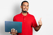 © Krakenimages.com - Young african american man working using computer laptop smiling happy and positive, thumb up doing excellent and approval sign