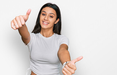 Young hispanic girl wearing casual white t shirt approving doing positive gesture with hand, thumbs up smiling and happy for success. winner gesture.