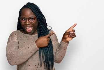 Wall Mural - Young black woman with braids wearing casual clothes and glasses smiling and looking at the camera pointing with two hands and fingers to the side.