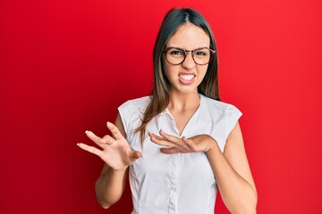 Wall Mural - Young brunette woman wearing casual clothes and glasses disgusted expression, displeased and fearful doing disgust face because aversion reaction. with hands raised