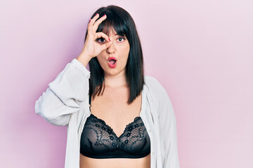 Canvas Print - Young hispanic woman wearing lingerie doing ok gesture shocked with surprised face, eye looking through fingers. unbelieving expression.