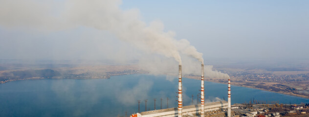 Aerial view of high chimney pipes with grey smoke from coal power plant. Production of electricity with fossil fuel.