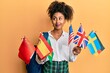 Beautiful african american woman with afro hair exchange student holding countries flags smiling looking to the side and staring away thinking.