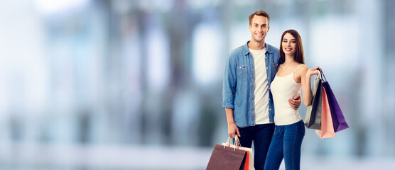 Wall Mural - Love, holiday sales, shop, retail, consumer concept - happy amazed couple with shopping bags. Blurred modern interior or mall background.