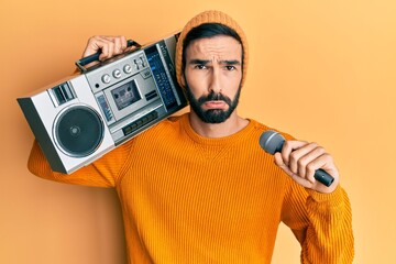 Wall Mural - Young hispanic man holding boombox, listening to music singing with microphone depressed and worry for distress, crying angry and afraid. sad expression.