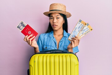 Poster - Young chinese woman holding boarding pass and passport clueless and confused expression. doubt concept.