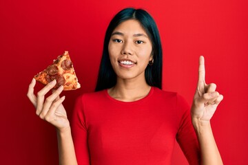 Poster - Young chinese woman holding italian pizza surprised with an idea or question pointing finger with happy face, number one