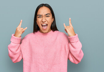 Wall Mural - Young asian woman wearing casual winter sweater shouting with crazy expression doing rock symbol with hands up. music star. heavy music concept.
