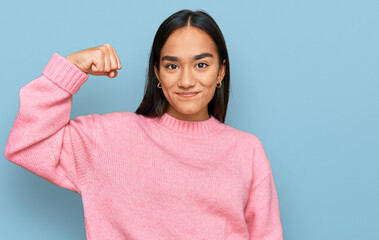 Wall Mural - Young asian woman wearing casual winter sweater strong person showing arm muscle, confident and proud of power