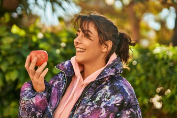 Young hispanic sporty woman smiling happy eating red apple at the park.