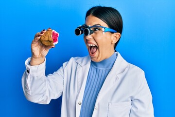 Sticker - Beautiful brunette jeweller woman holding geode stone wearing magnifier glasses celebrating crazy and amazed for success with open eyes screaming excited.