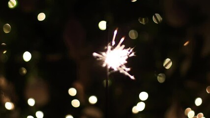 Wall Mural - Beautiful burning firework in dark room on background of golden lights bokeh on christmas tree. Happy New Year and Merry Christmas concept. Burning sparkler, bengal light. New year Party