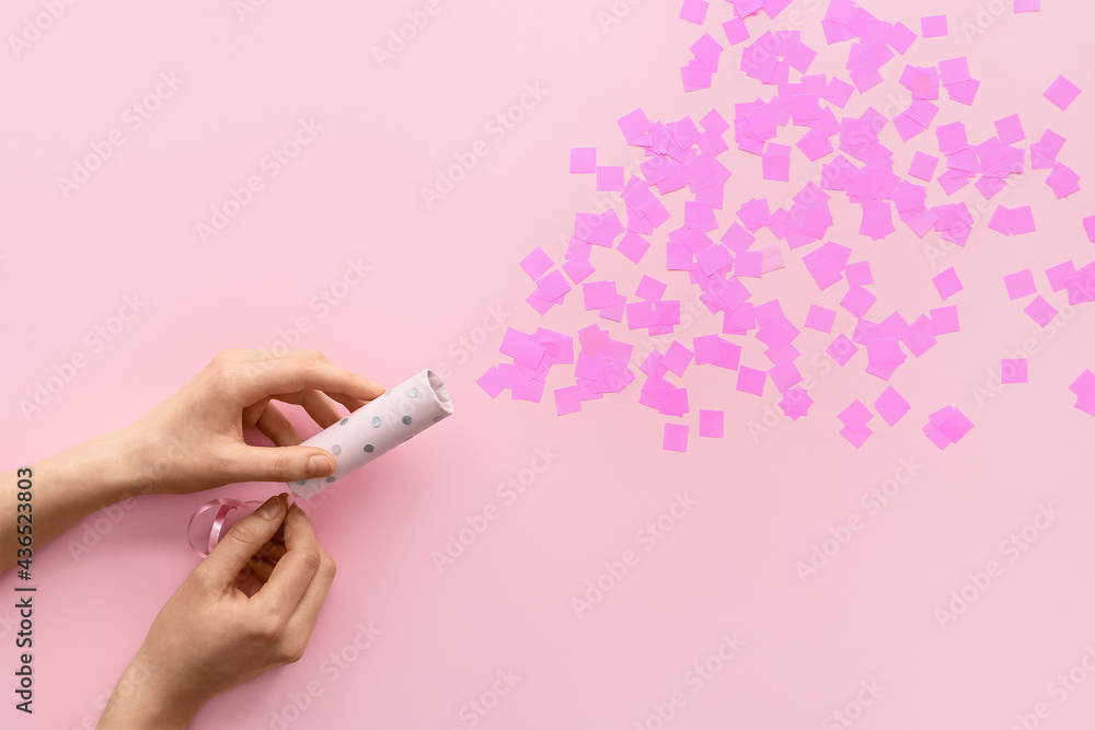 Female hands with party popper and confetti on color background