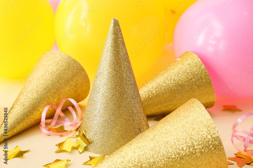 Party cones with confetti and air balloons on color background
